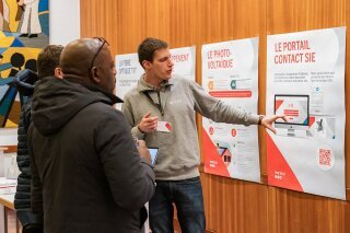 Intervenant et participant devant un stand d'informations SIE lors de la conférence publique des SIE « L'avenir du solaire en Suisse »
